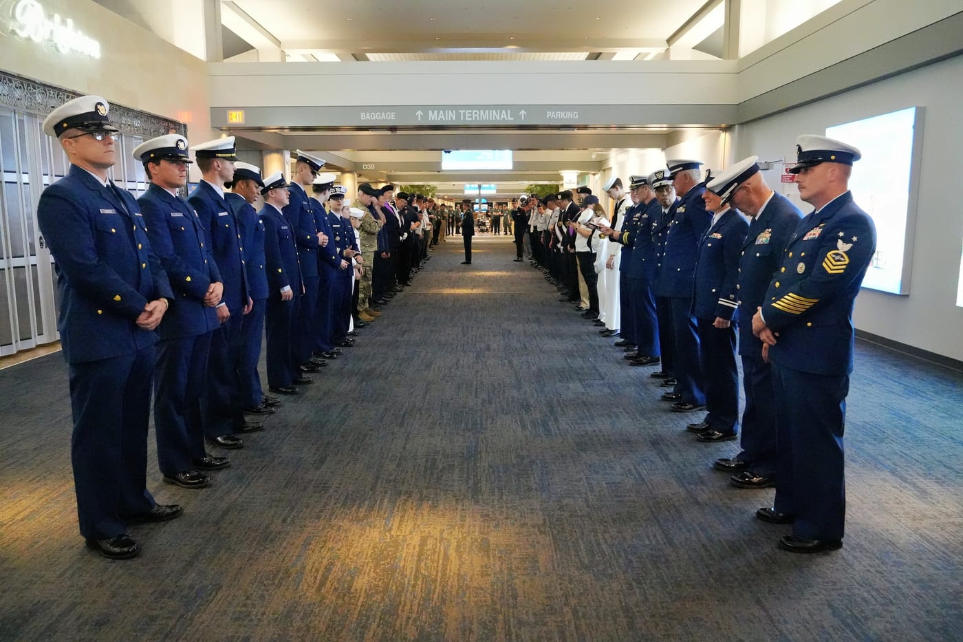 Two lines of military personnel standing at attention in a formal ceremony at an airport terminal