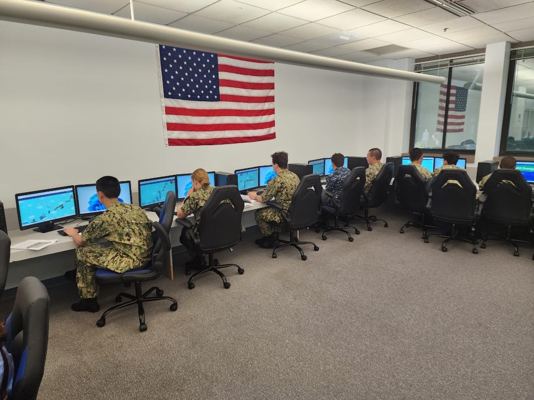 Cadets including Kendra Ugoretz working at computers during cybersecurity training under an American flag